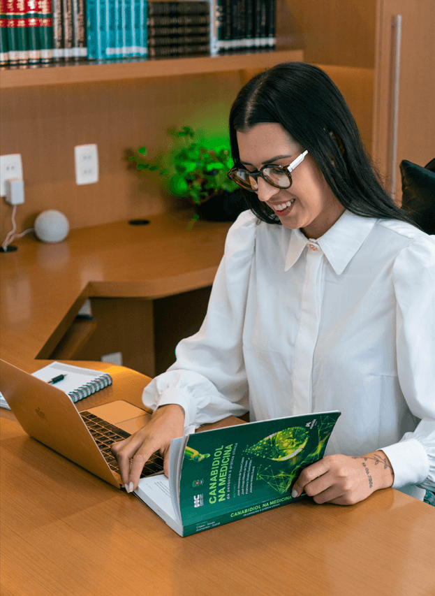 Brunna Varela em seu escritório, com um livro sobre cannabis medicinal.